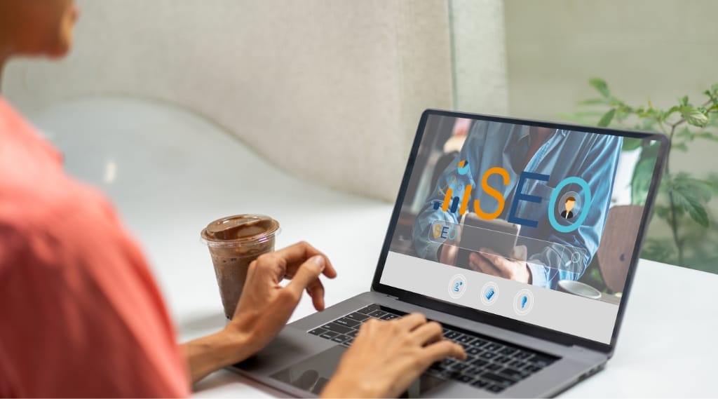 A woman works on a laptop which reads 'SEO' on the screen