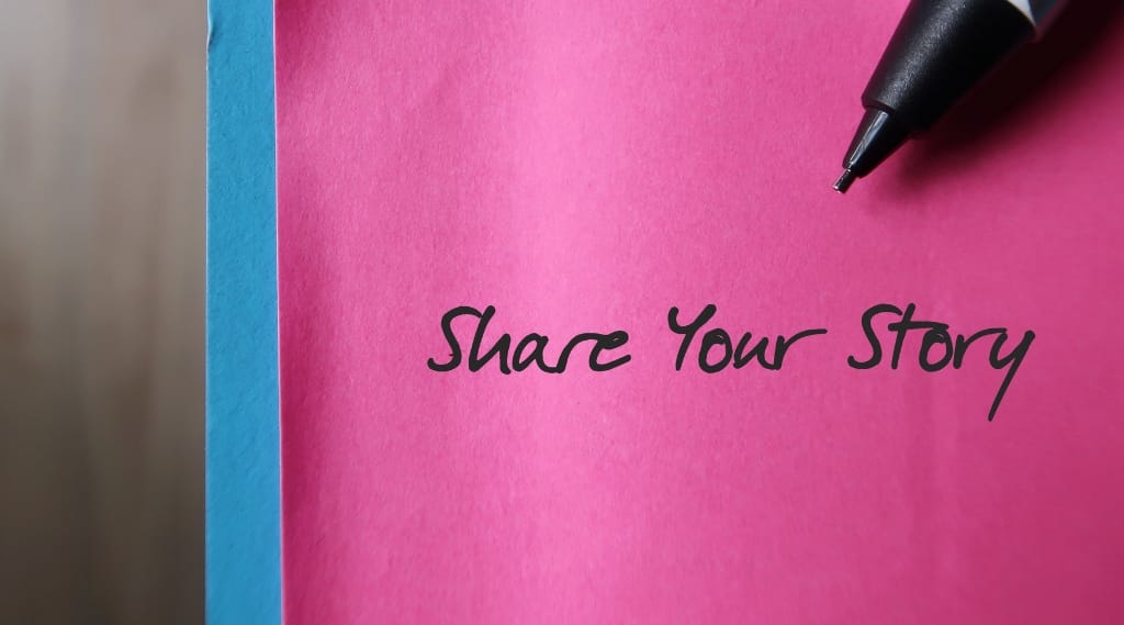 A pen writes 'share your story' on a pink post it note
